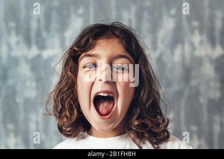 ritratto di una bambina che grida forte su uno sfondo blu, infanzia felice e concetto di stile di vita Foto Stock