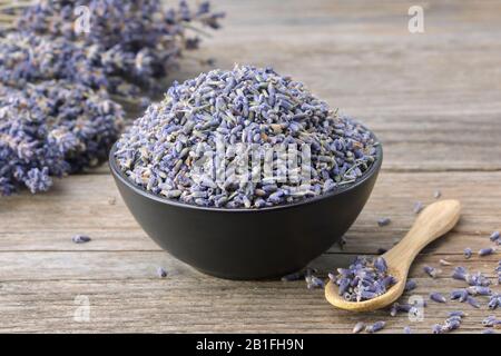 Ciotola nera di fiori secchi di lavanda e mazzo di lavanda su tavolo di legno. Foto Stock