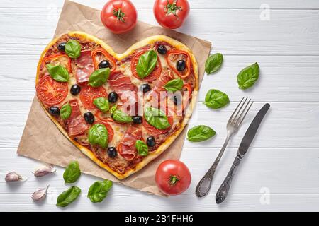 Prosciutto a forma di cuore pizza caldo amore concetto San Valentino design simbolo romantico ristorante cena italiano cibo. Olive, pomodori, basilico e mozz Foto Stock