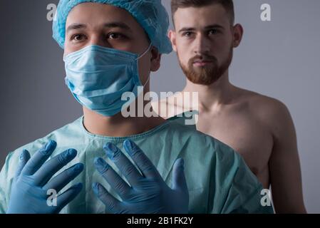 ritratto di closeup a fuoco di un chirurgo asiatico in maschera medica e vestaglia, guanti sterili, tenendo le mani sulla preparazione per il funzionamento. In defocu Foto Stock