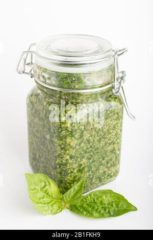 Salsa di pesto in un vaso di vetro isolato con foglie di basilico fresco su sfondo bianco. Tradizionale pesto di salsa italiana fatto in casa e basilico. Foto Stock