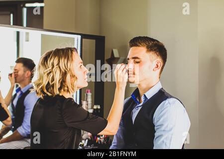 Makeup artista fare trucco professionale per il giovane uomo. Foto Stock