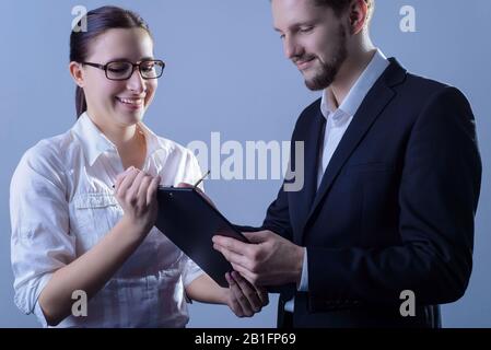 ritratto di due giovani uomini d'affari, in abiti d'affari, una donna d'affari tiene una cartella nella sua mano in modo che l'uomo d'affari segni. Studio foto su un g Foto Stock