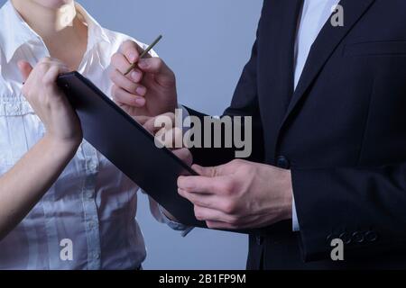 ritratto di due giovani uomini d'affari, in abiti d'affari, una donna d'affari tiene una cartella nella sua mano in modo che l'uomo d'affari segni. Studio foto su un g Foto Stock