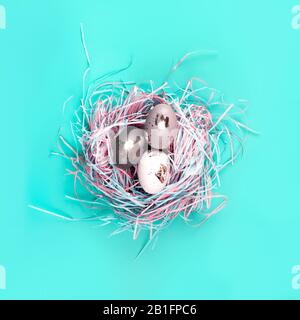 Nido ornitologico decorativo con creative uova d'argento dipinte a mano su sfondo pastello blu. Concetto di Pasqua. Stile a disposizione piatta. Foto Stock