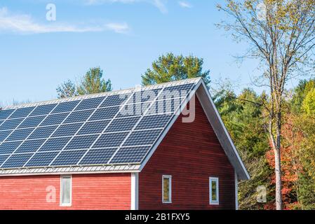 Tetto di un tradizionale fienile di legno rosso americano coperto con pannelli solari in una giornata di autunno soleggiato Foto Stock