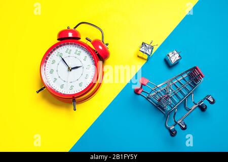 Sveglia rossa, piccolo carrello per lo shopping su sfondo a colori. Concetto di shopping Foto Stock
