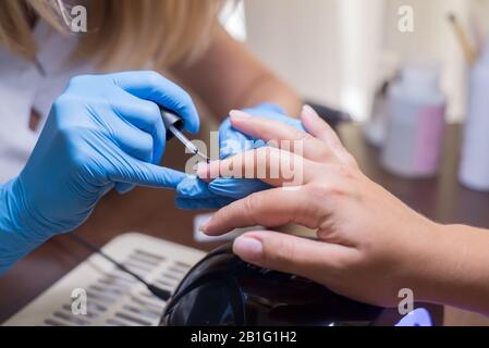 Capitano donna manicure. La ragazza non manicure in un salone di bellezza. Sotto una lampada da tavolo, in un ufficio, closeup mani e unghie di verniciatura Foto Stock