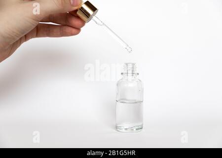 La goccia di acido ialuronico cade dalla pipetta cosmetica su sfondo bianco, Flacone in vetro contagocce Mock-Up Foto Stock