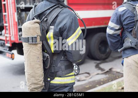 Primo piano di un vigile del fuoco con un cilindro di un estintore. Contro lo sfondo di un rosso fuoco motore. Pericolo di incendio. È possibile vedere la carbonizzazione interior de Foto Stock