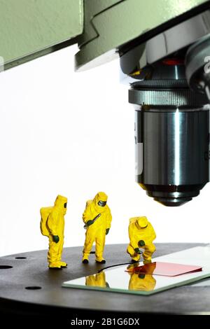 Immagine concettuale della figura in miniatura persone che indossano abiti Hazmat guardando un campione di sangue falso sotto un microscopio Foto Stock