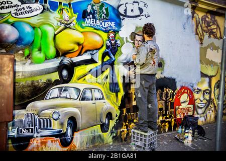 Young man, artista al lavoro che dipinge un murale raffigurante i temi simbolo di Melbourne, Richmond, Melbourne, Victoria, Australia Foto Stock