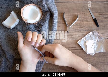 Cura delle mani, folk cura delle mani. Manicure con olio di noce di cocco, manicure strumenti: Forbici, lima per unghie. Foglio per la rimozione di gel polish su sfondo di legno. La bellezza di un Foto Stock