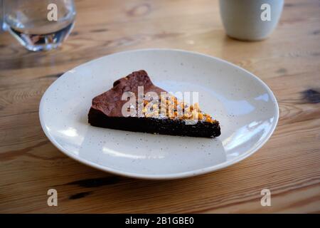 Una semplice piastra bianca con una fetta di tortino al cioccolato ricoperto di buccia d'arancia Foto Stock