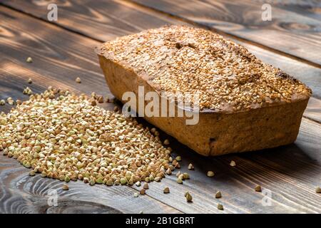 Utile pane di grano saraceno con crosta dorata e un mazzo di grani verdi vicino su un tavolo di legno. Cibo vegano e vegetariano. Deliziosi dolci fatti Foto Stock