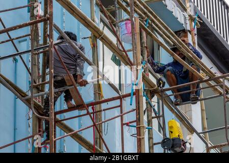 Ponteggi che lavorano su una struttura alta in Thailandia senza imbracature di sicurezza o attrezzature per la salute e la sicurezza che mettono a rischio di caduta. Foto Stock