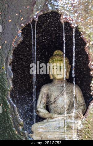 un dio buddista buddha o divinità in una grotta di pietra con una cascata e acqua corrente che cade dalle rocce in thailandia, asia. Foto Stock