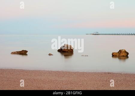 Tramonto rosa sul mare calmo. Pietre in primo piano. Pietre e mare con lunga esposizione. Acqua rilassante Foto Stock