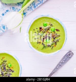 Stagione degli asparagi. Zuppa di crema verde fatta in casa con asparagi, piselli verdi, semi di sesamo neri e olio di zucca su sfondo bianco Foto Stock
