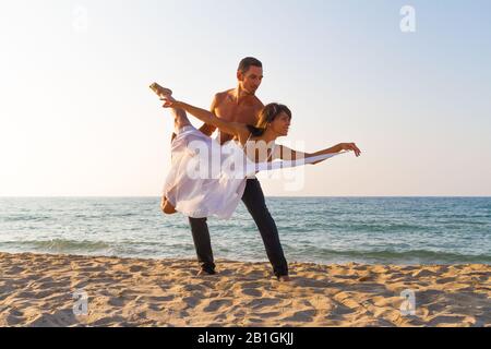 Atletica giovane coppia in spiaggia esercizi di fitness ACro yoga pratica, equilibrio in coppia in una giornata estiva al tramonto. Uno stile di vita sano Foto Stock