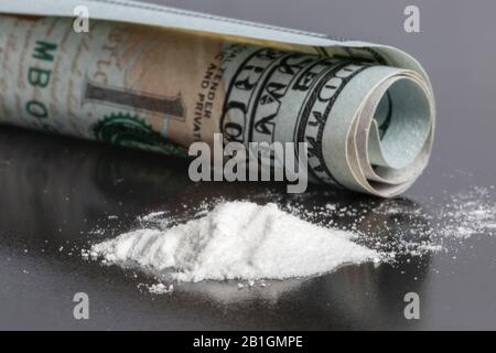 Ha rotolato cento dollari banconote e cocaina su sfondo nero. Concetto di tossicodipendenza e abuso di sostanze. Foto Stock