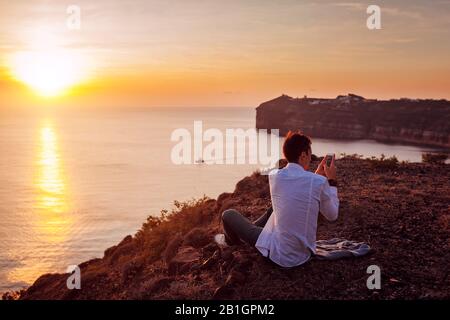 Turistica scattare foto del paesaggio di montagna di mare usando lo smartphone sull'isola di Santorini. Uomo in viaggio. Vacanze estive Foto Stock