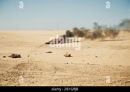 Il fuoco e il fumo pesante nel deserto vicino all'insediamento durante la siccità. Combustione di rifiuti e plastica Foto Stock