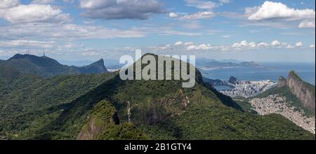 Panorama di Rio de Janeiro con parte del parco nazionale tropicale di Tijuca in primo piano e più ampio paesaggio urbano sullo sfondo di un cielo blu Foto Stock