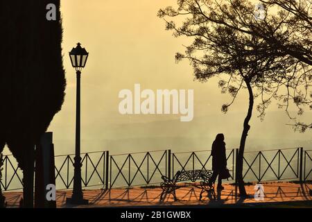 Silhouette di una donna solitaria che cammina attraverso il parco con una speciale luce del tramonto Foto Stock