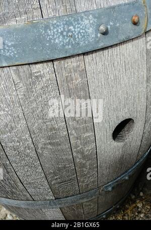 Primo piano del foro di tappo in vecchia botte di legno grigio tra bande metalliche colorate. Foto Stock