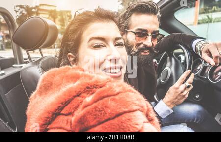 Felice coppia trendy divertirsi all'interno di auto convertibile in giro per la città durante l'inverno - Paesaggio Urbano, viaggio e concetto di rapporto - Focus su donna Foto Stock