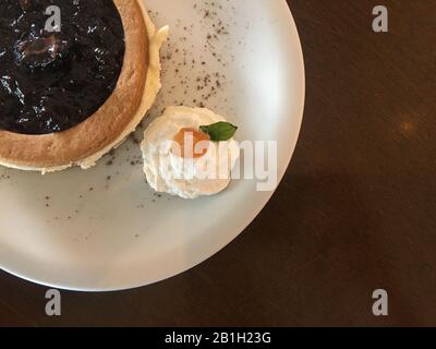 Primo piano di deliziosi cheesecake blackberry con panna montata e albicocca nell'angolo della piastra bianca in ceramica su un tavolo in legno. Foto Stock