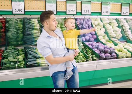 Padre caucasico che acquista in negozio di alimentari con figlio bambino. Papà che acquista verdure fresche. Uomo genitore con bambino che sceglie pasto sano per LUN di spuntino Foto Stock