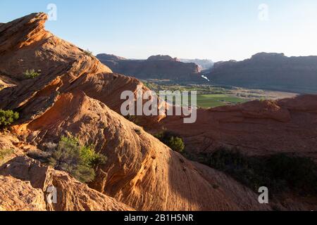 Il Bureau of Land Management ha annunciato il 24 febbraio che avrebbe rimosso due pacchi di terra all'interno del Sand Flats Special Recre 5 aprile 2015 - Moab, Utah, Stati Uniti - Vista da slick percorso di roccia di campi verdi e terreni agricoli con il fiume Colorado e canyon dietro. Lo Slickrock Trail, è una popolare destinazione per mountain bike con fama mondiale. Questo percorso di 20,9 km porta intrepidi piloti su un paesaggio di dune di sabbia "pietrificate" e i resti erosi di antiche aiuole marine. Il sentiero di Slickrock è una delle più difficili passeggiate nella zona di Moab, sia tecnicamente che cardiovascolarmente, e. Foto Stock