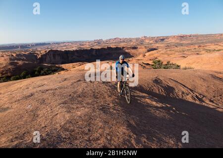 Il Bureau of Land Management ha annunciato il 24 febbraio che avrebbe rimosso due parcelle di terra all'interno del Sand Flats Special Recre 5 aprile 2015 - Moab, Utah, Stati Uniti - Mountain biker a cavallo della arenaria rossa del famoso percorso di roccia calcarea con il fiume Colorado e canyon dietro. Lo Slickrock Trail, è una popolare destinazione per mountain bike con fama mondiale. Questo percorso di 20,9 km porta intrepidi piloti su un paesaggio di dune di sabbia "pietrificate" e i resti erosi di antiche aiuole marine. Il sentiero di Slickrock è una delle più difficili corse nella zona di Moab, sia tecnicamente che cardiovascu Foto Stock