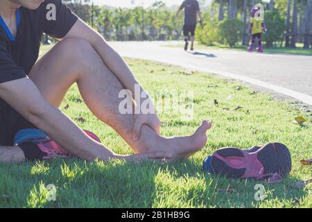 Caviglia slogata. Giovane uomo che soffre di una caviglia infortunata durante la corsa in posizione di parcheggio. Assistenza sanitaria e sport concept. Foto Stock