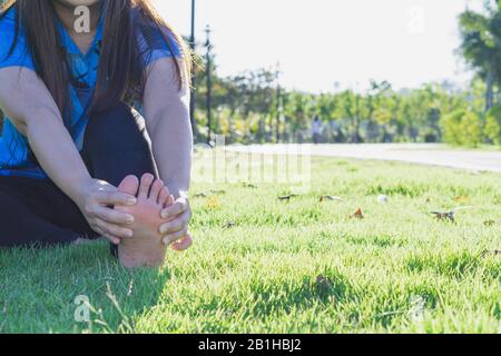 Giovane donna massaggiare il suo piede doloroso da jogging e in esecuzione nel parco. Lo sport e il concetto di esercizio. Foto Stock