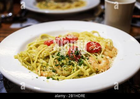 Linguine al pesto fatte in casa con gamberi saltati mescolati con basilico organico, pinoli e mandorle mescolati in salsa Alfredo e guarniti con pomodori d'uva Foto Stock
