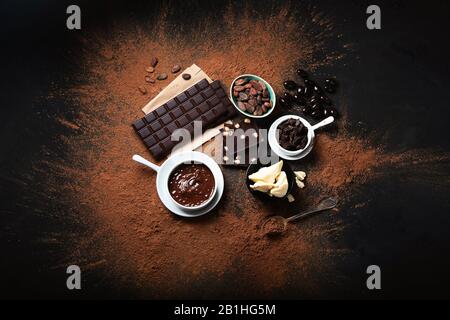 Barra di cioccolato fondente, pezzi di cioccolato e fave di cacao, polvere di cacao su sfondo nero. Vista dall'alto Foto Stock