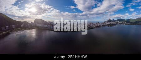 Panorama aereo a 180 gradi del lago Lagoa Rodrigo de Freitas città di Rio de Janeiro con cielo blu intenso e sole dietro una nuvola sopra Ipanema Foto Stock