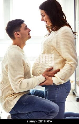Primo piano ritratto di aspettare coppia adolescente ridere felicemente, abbracciando il bambino nel ventre insieme. Coppia vestita di colori blu e bianco Foto Stock