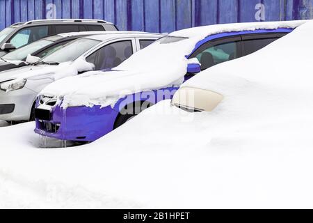 Auto in un parcheggio sotto la neve accanto a una recinzione viola. Confisca dei veicoli. Concetto di vacanza in paesi caldi con un'auto parcheggiata per un lungo periodo Foto Stock