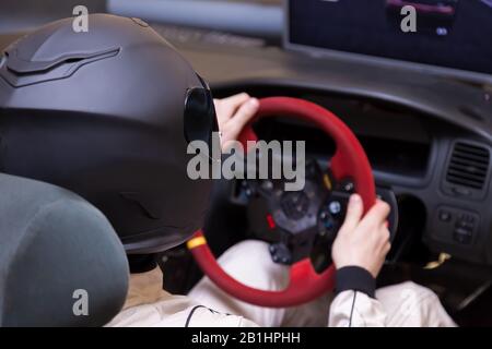 Un corridore professionista in un casco nero e una tuta omologata bianca siede nel sedile sportivo di una vettura per la guida e le corse durante una corsa e un tirocinio Foto Stock