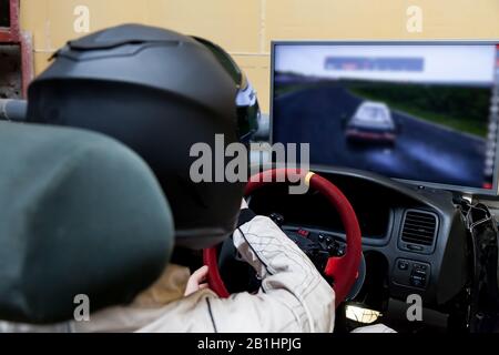 Un corridore professionista in un casco nero e una tuta omologata bianca siede nel sedile sportivo di una vettura per la guida e le corse durante una corsa e un tirocinio Foto Stock