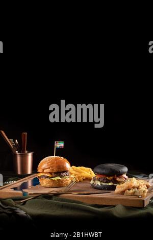 due hamburger neri e di livello con carne e sesamo con patate fritte servite su tavole di legno Foto Stock