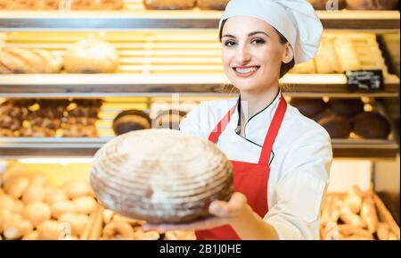 Commessa con grembiule presentando il pane fresco in un panificio Foto Stock