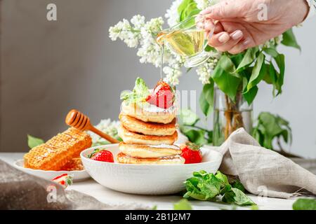 Miele versato su una pila di mini frittelle con fragola Foto Stock