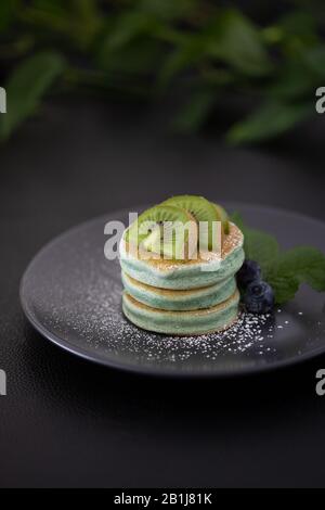 Frittelle verdi su un tavolo nero con kiwi verde Foto Stock