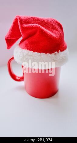 cappello rosso di natale vestito su una tazza rossa su sfondo bianco Foto Stock