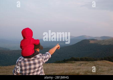 Papà con figlio sulle montagne primaverili seduto in erba alta. Famiglia campeggio. Viaggi con concetto di bambino Foto Stock